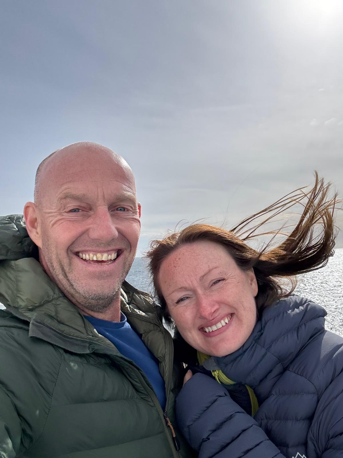 Dave and Lindsey in a windswept selfie on the ferry deck, open sea behind, on the calm Bay of Biscay crossing.