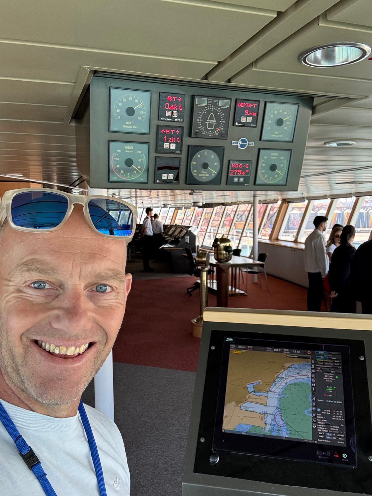 Dave on the ship's bridge with the crew and navigation instruments, wearing a visitor lanyard.