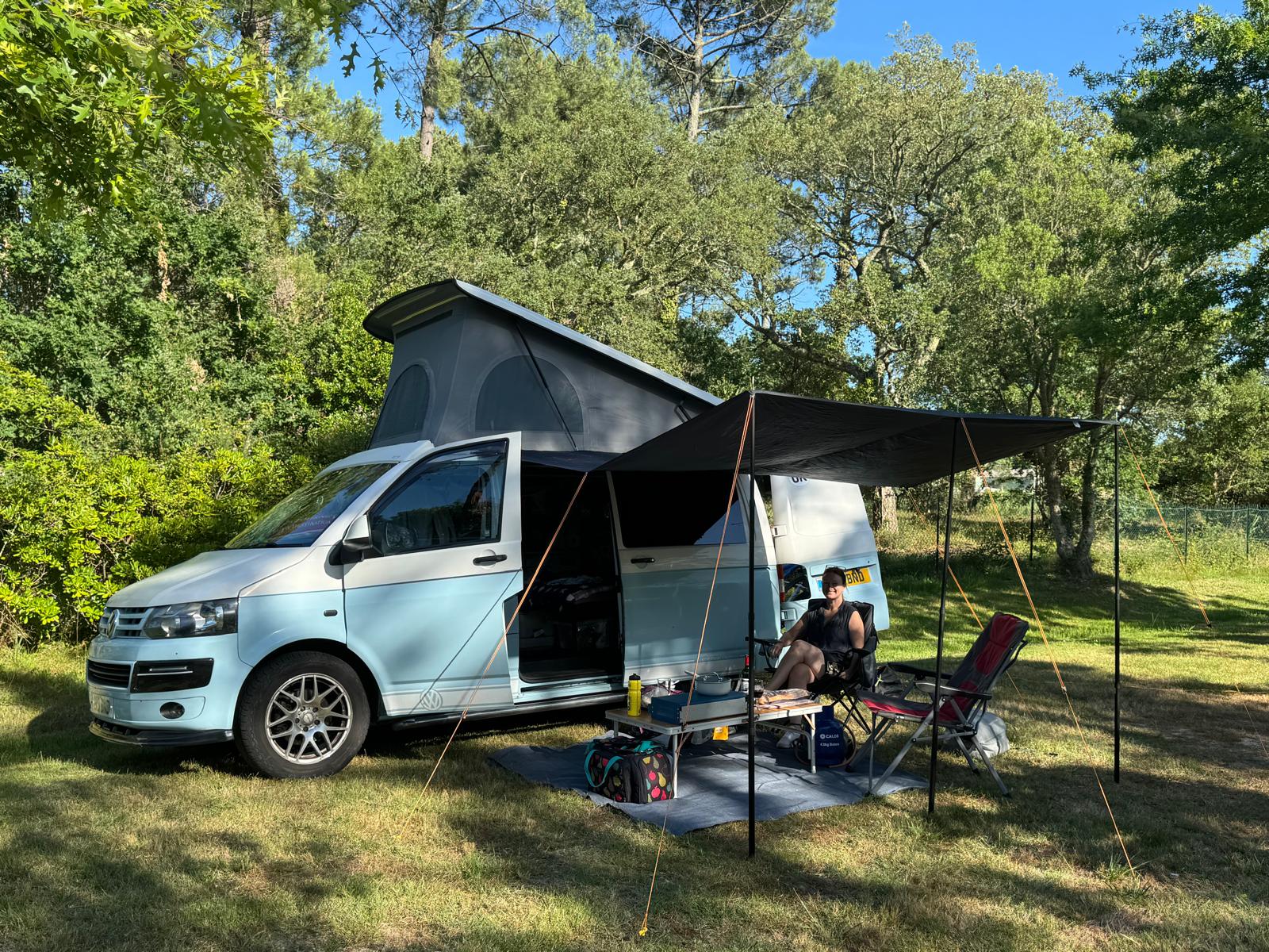 The campervan pitched among the trees at Messanges, roof up and awning out, bikes on the back.