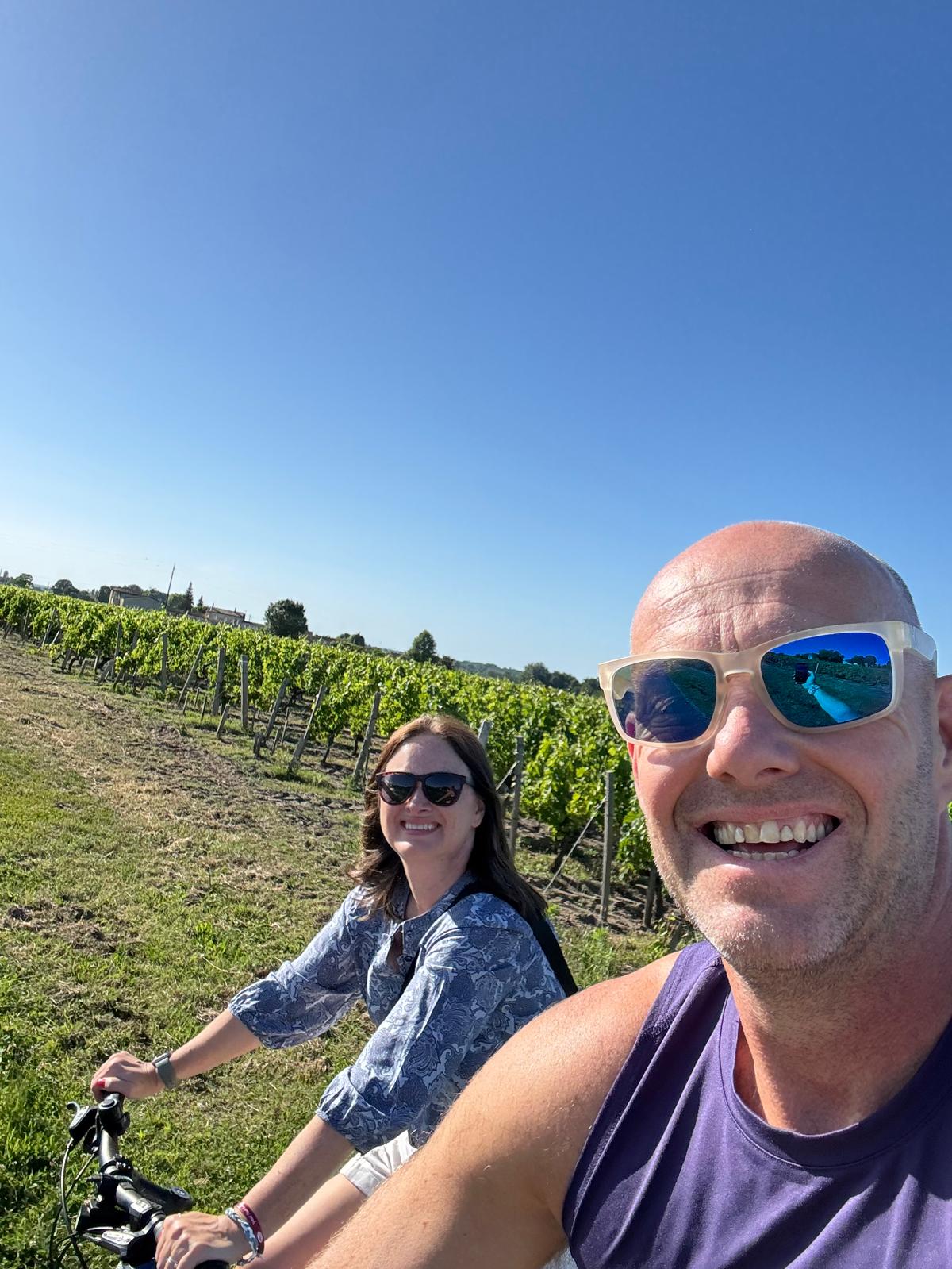 Dave and Lindsey on bikes in the vineyards near Saint-Émilion, both grinning.