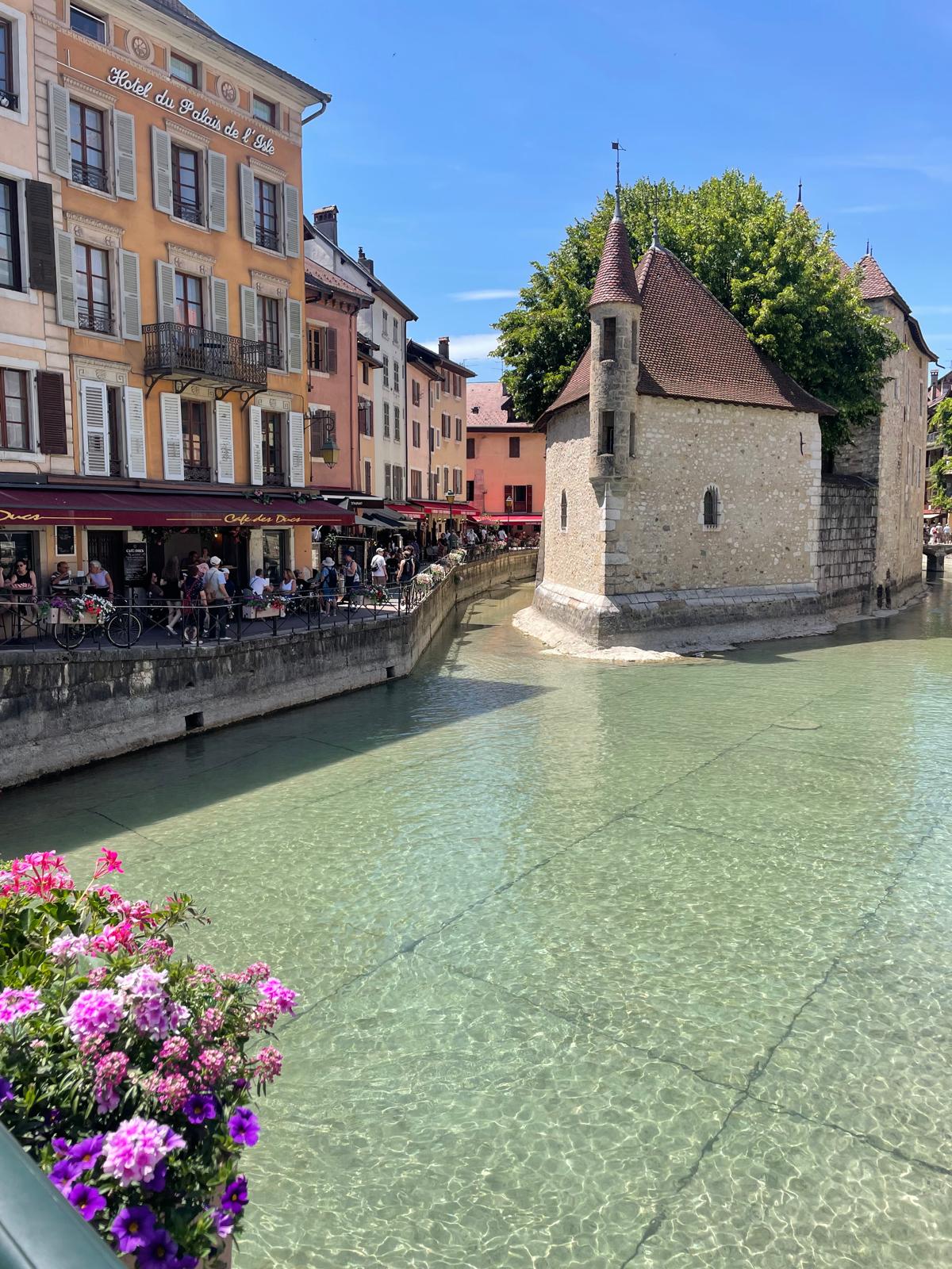 The boat-shaped medieval Palais de l’Île sitting mid-canal in Annecy, turquoise water around it.