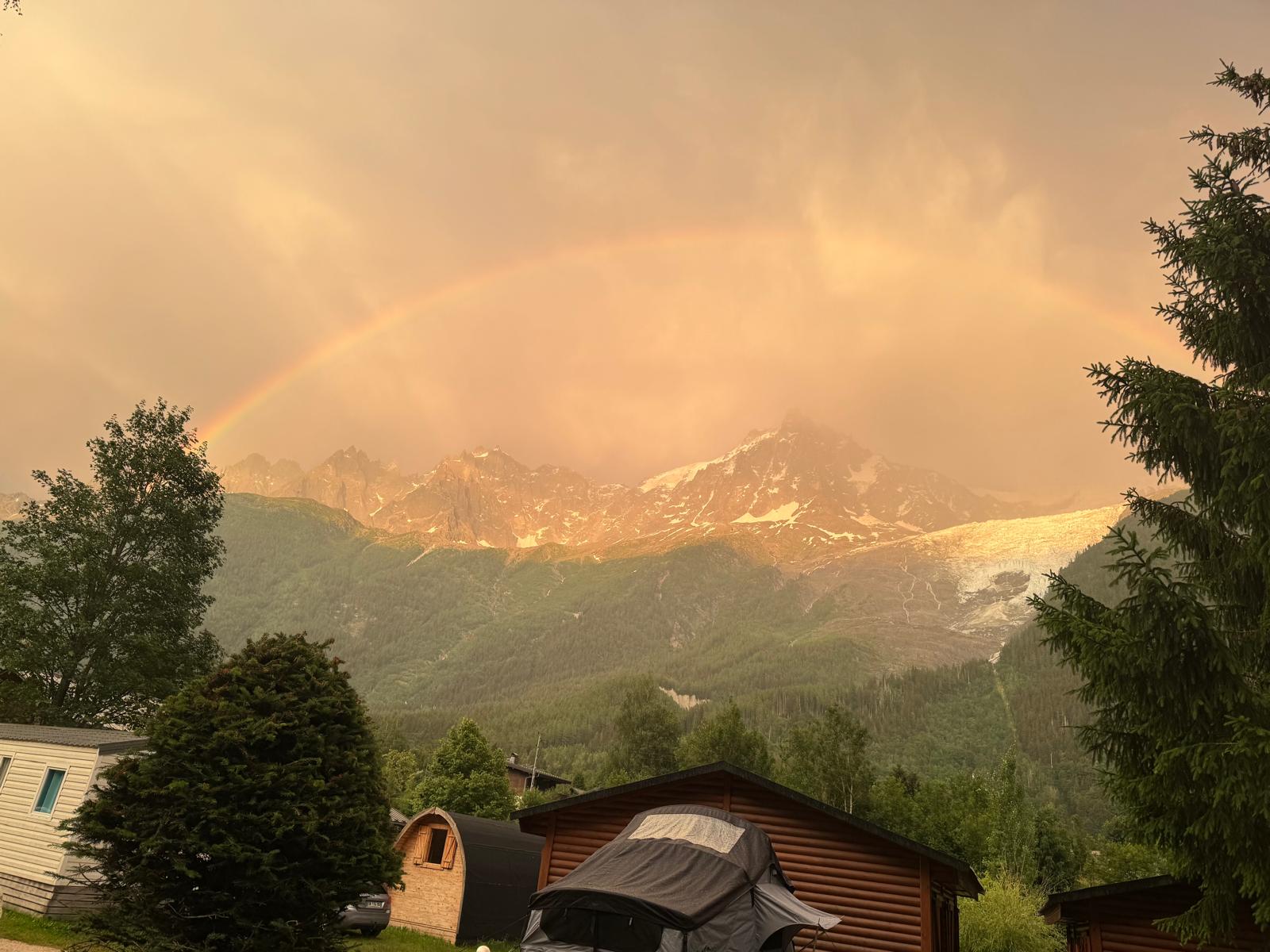 A full rainbow arcing over the snow-streaked Aiguilles above the Chamonix campsite after a storm.