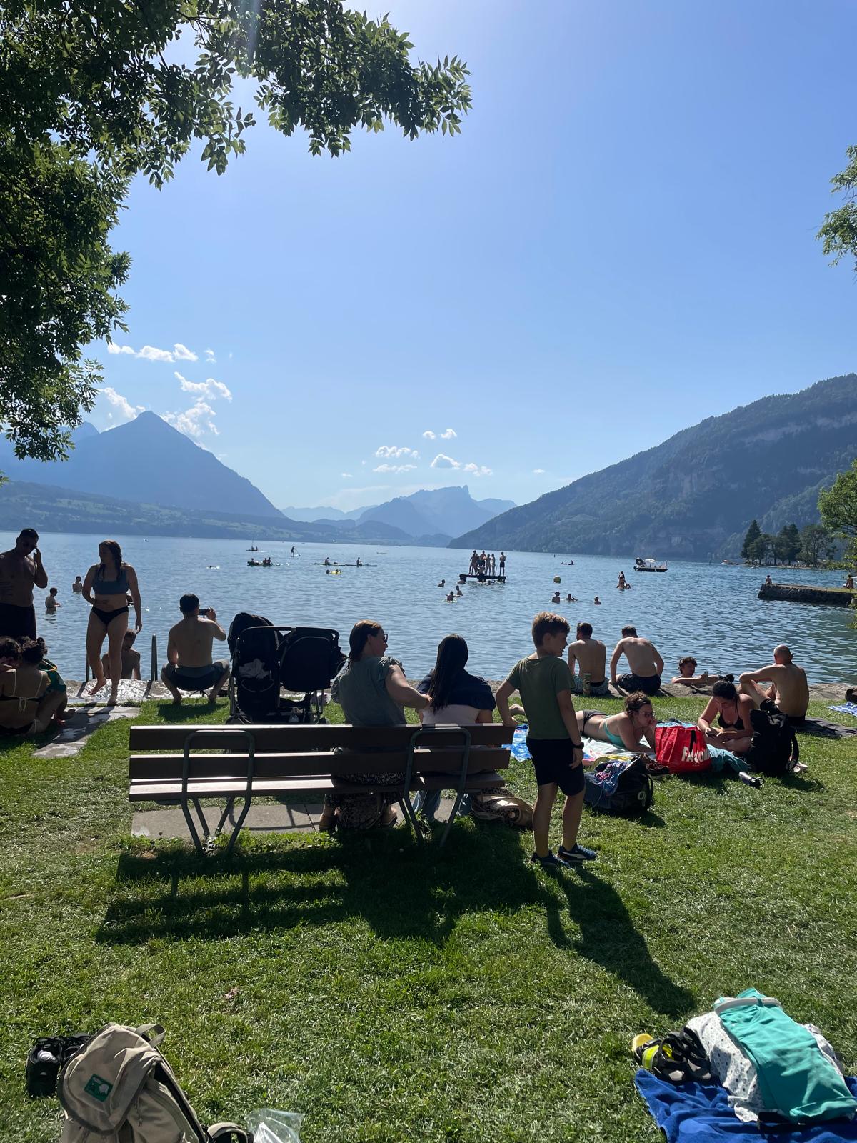 A busy lakeside beach near Interlaken — swimmers, a floating platform and sunbathers, the lake ringed by mountains.