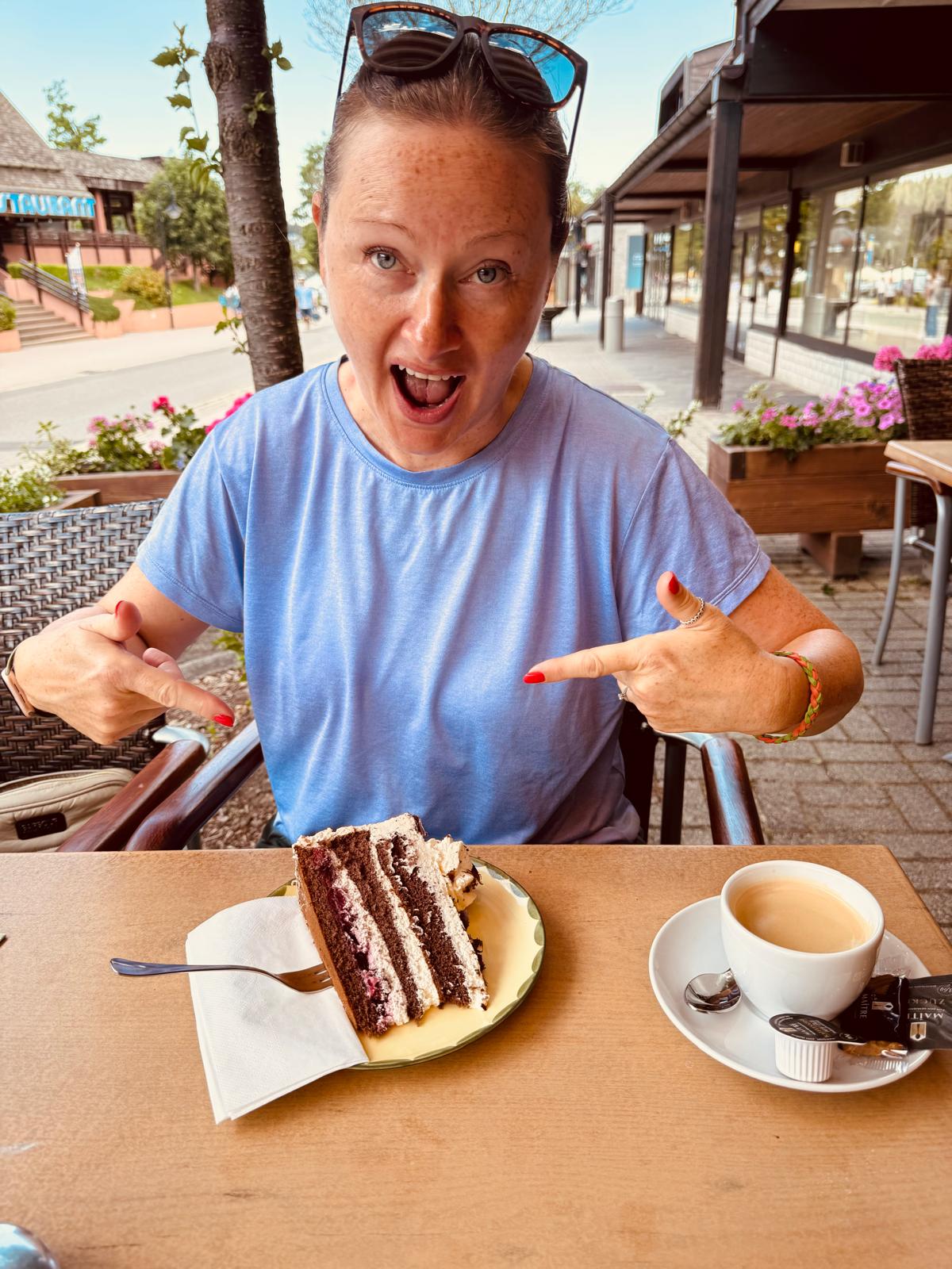 Lindsey pointing delightedly at a tall slice of Black Forest gâteau on a café table.