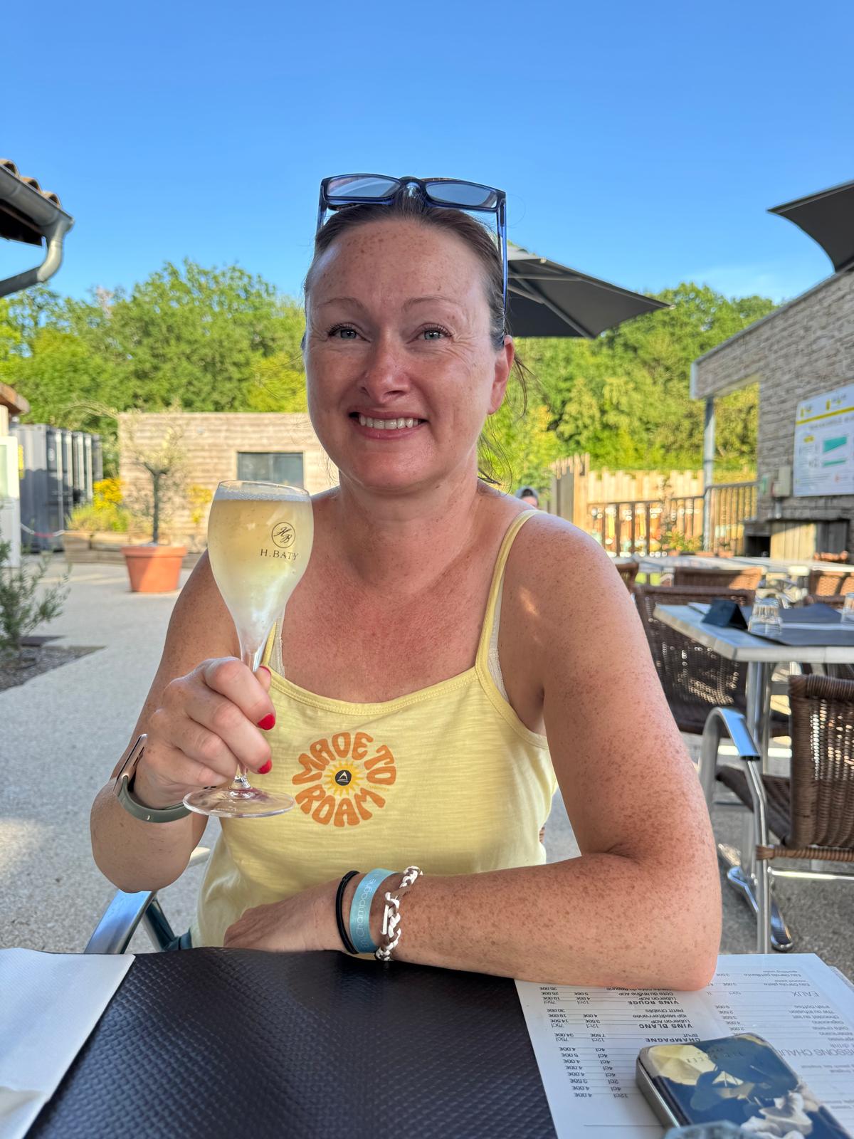 Lindsey raising a champagne flute at a sunlit terrace, golden evening light.